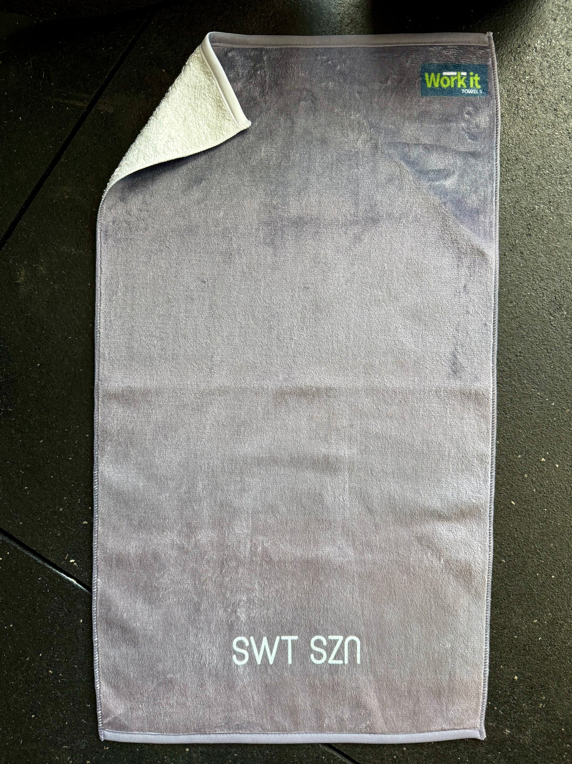 Gray towel with 'SWT SZN' branding on a dark surface