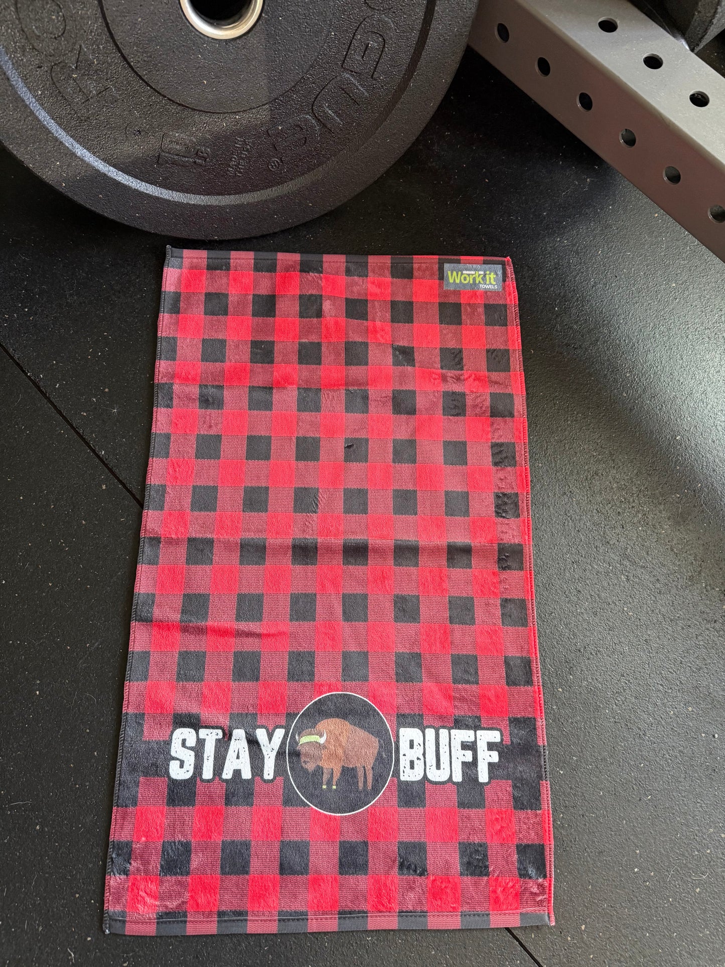 Red and black checkered towel with 'Stay Buff' text on a gym floor.