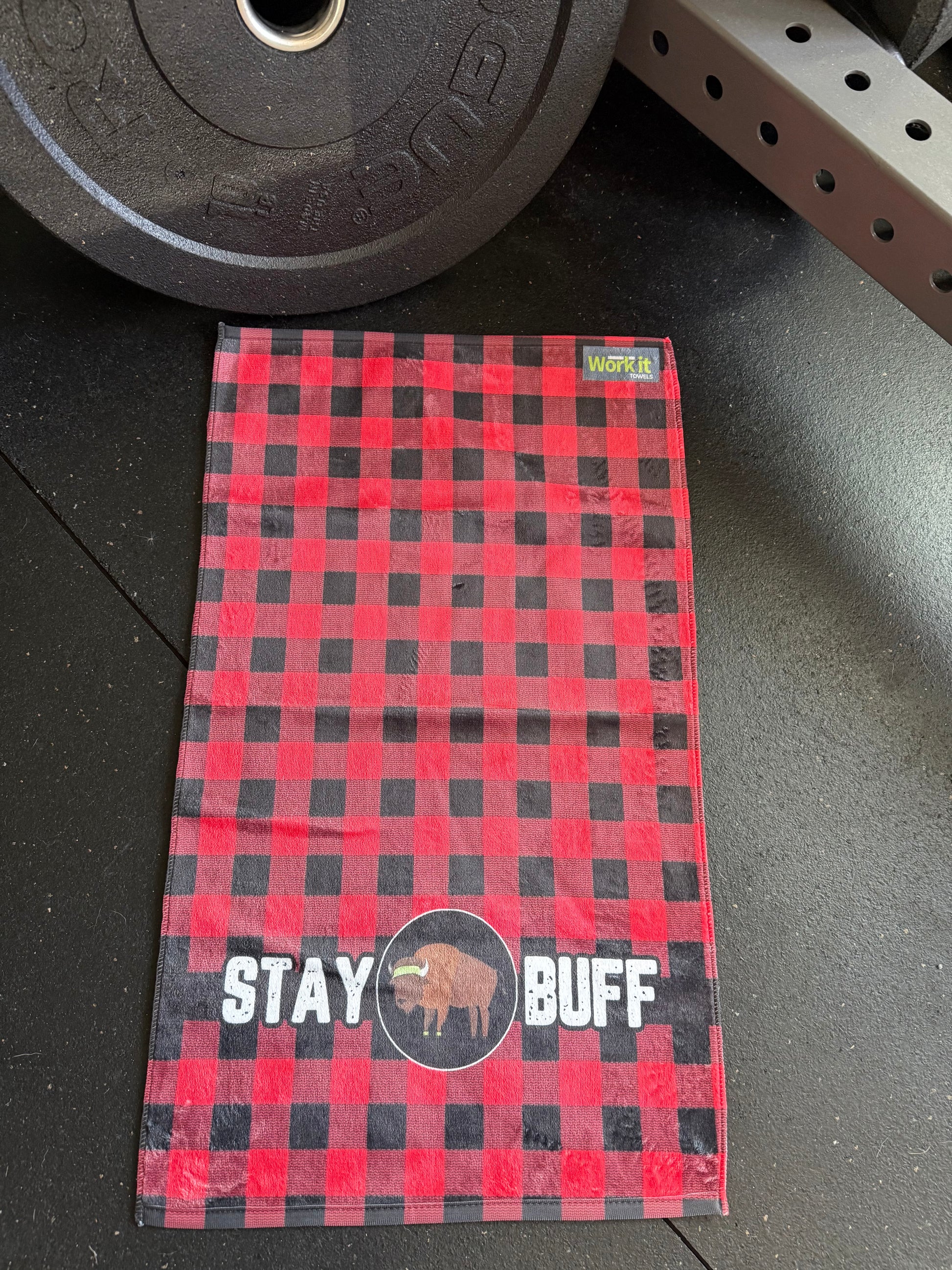 Red and black checkered towel with 'Stay Buff' text on a gym floor.