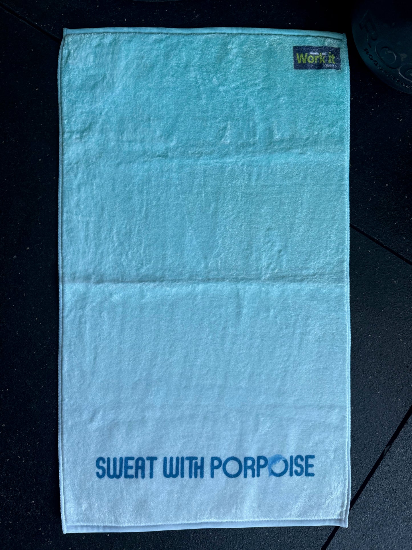 Teal towel with 'Sweat with Porpoise' text on a dark surface