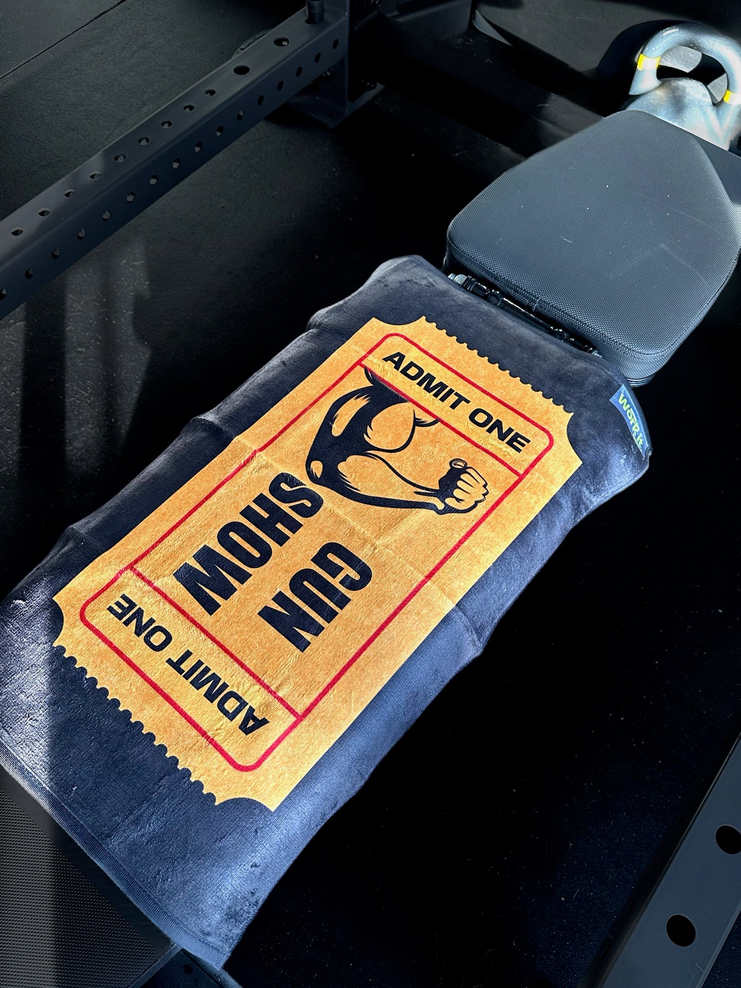 A workout bench featuring the 'ticket to the show' sweat towel with a flexing bicep