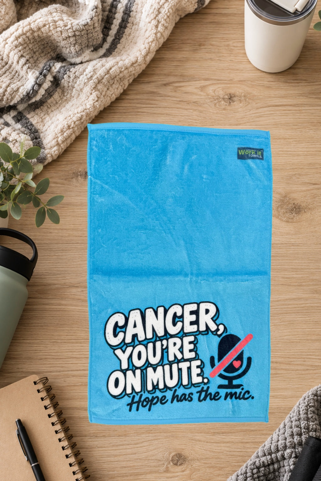 Blue Cancer, You're On Mute towel laid flat on a wood table beside a knit blanket, water bottle, tumbler and notebook.