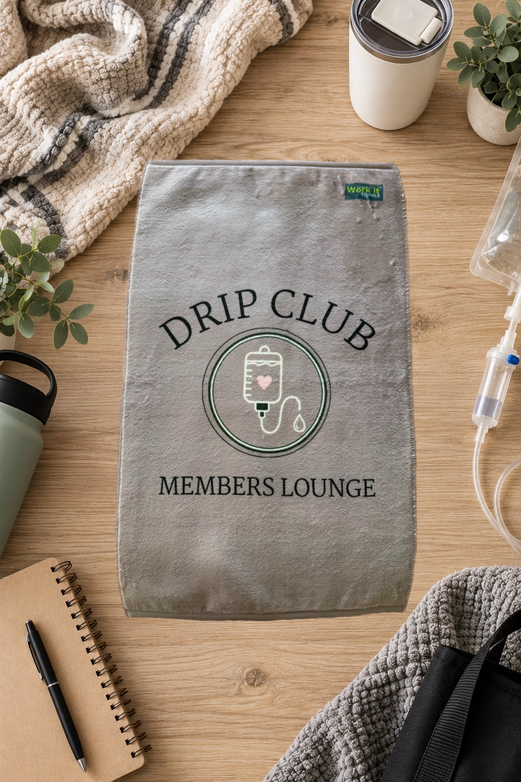 greyish mauve towel design with an IV and the font, 'drip club members lounge' on a hardwood floor with blankets and drinks 