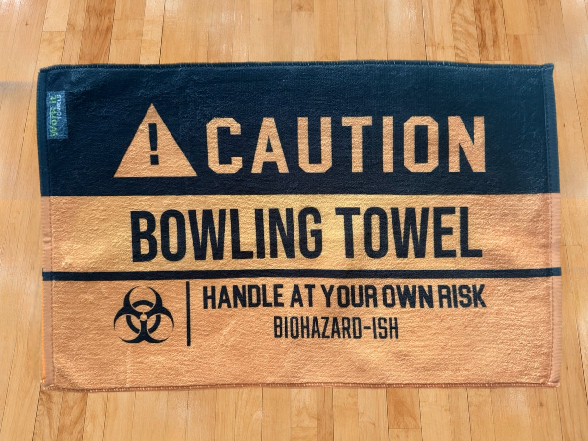 yellow and black caution towel  with 'caution bowling towel, handle at your own risk, biohazardish' on shiny hardwood bowling floor