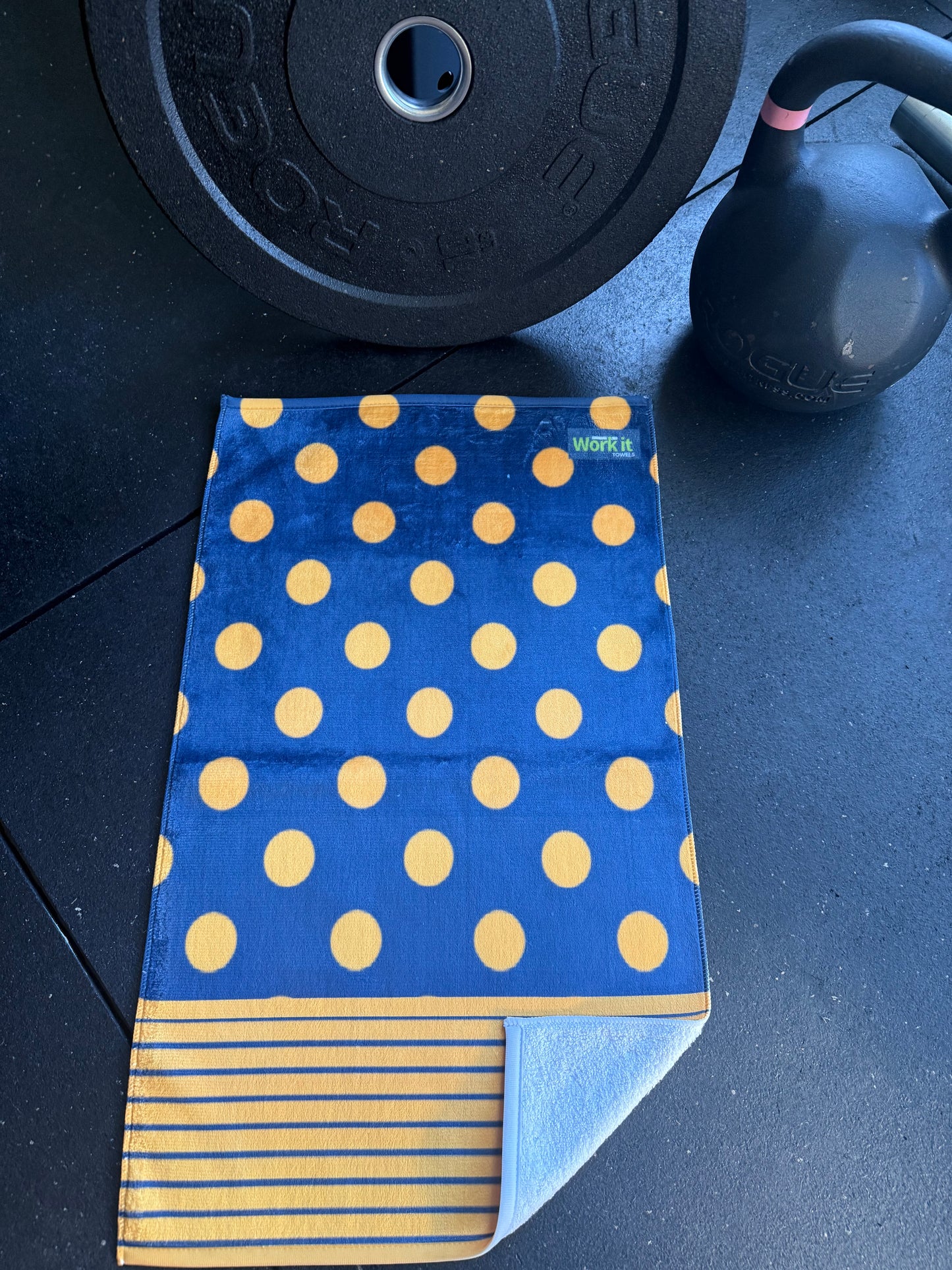 Blue towel with yellow polka dots and stripes next to a black weight on a dark surface