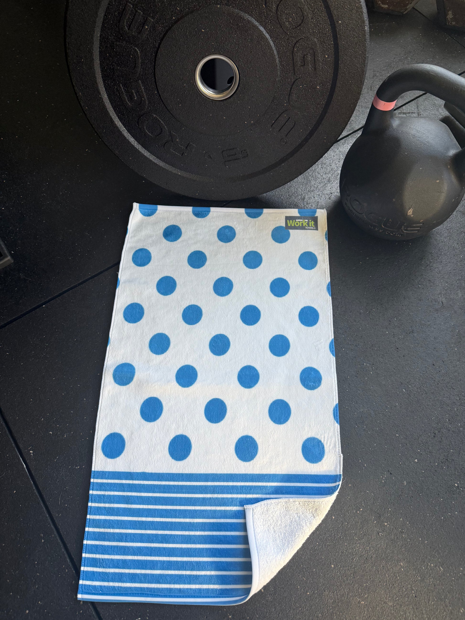 Blue polka dot towel on a black surface with gym equipment.