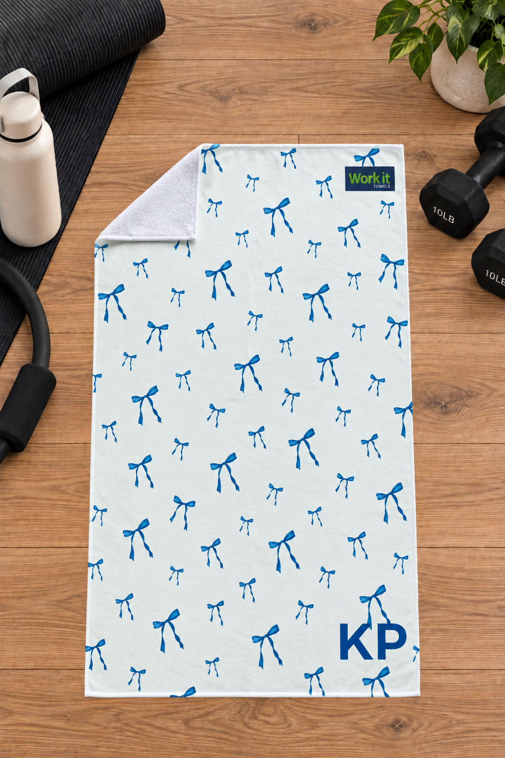 Blue bow personalized gym towel with custom 'KP' initials, one corner folded back to show the soft white terry reverse side.
