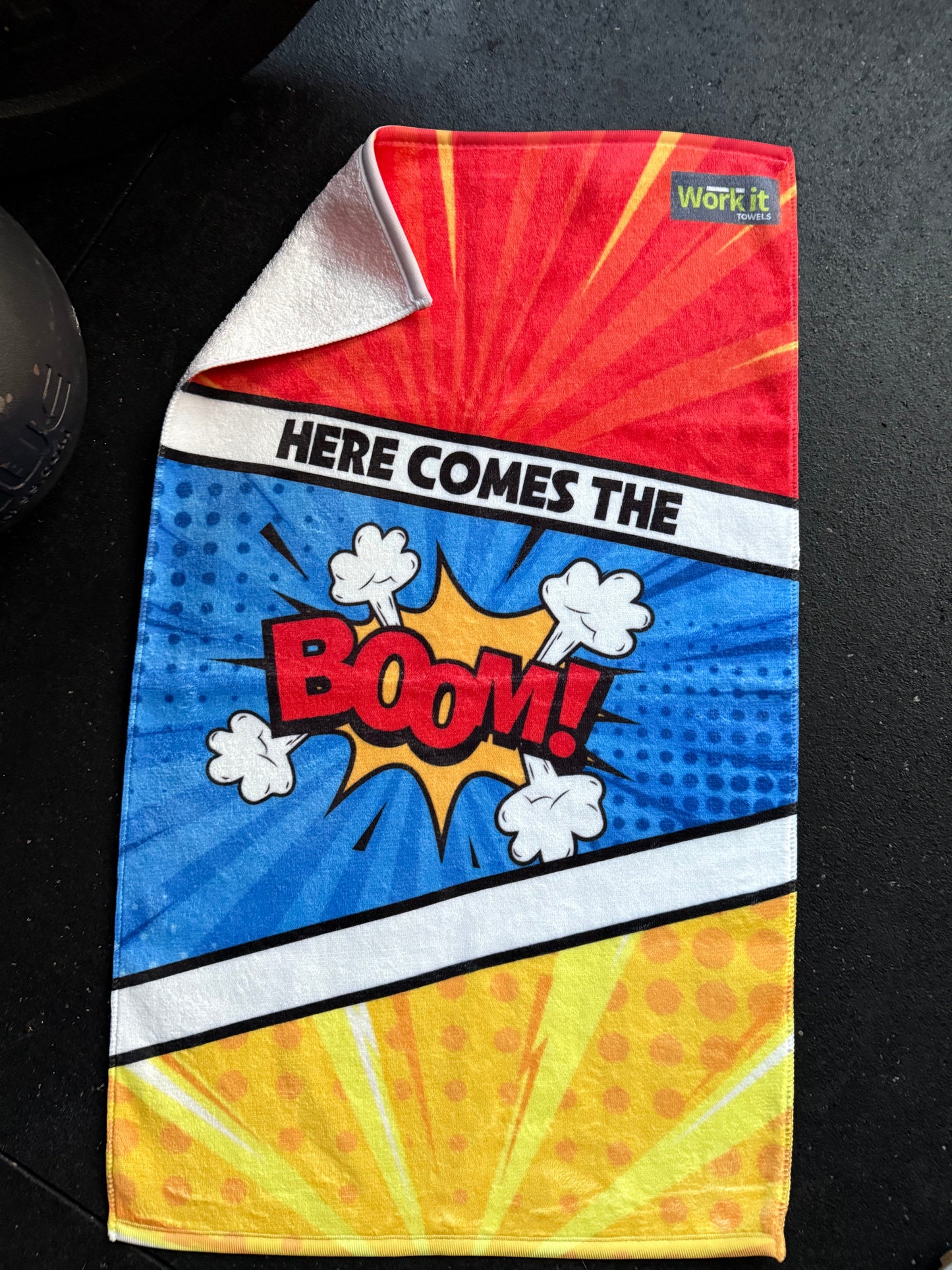 Colorful towel with comic book-style design featuring the word 'BOOM!' on a black surface.