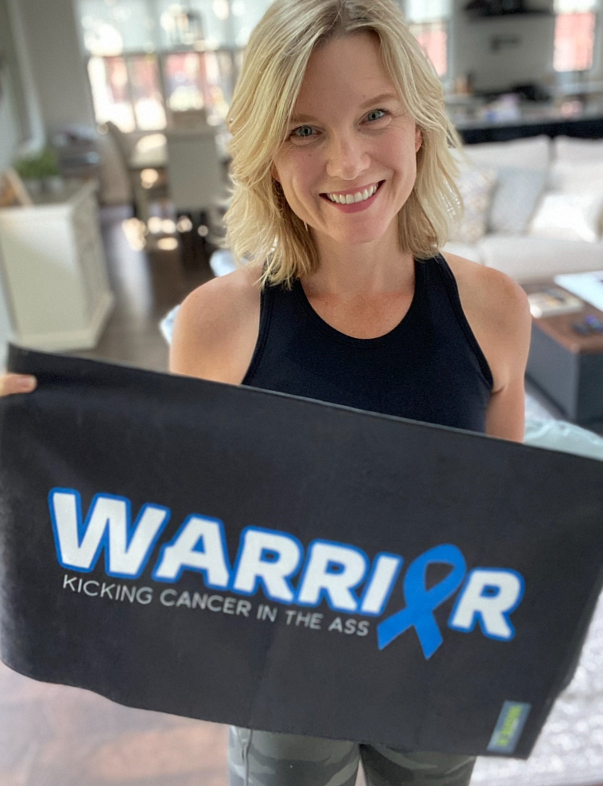 Person holding a black pillow with 'Warrior' and a blue ribbon design in a living room.