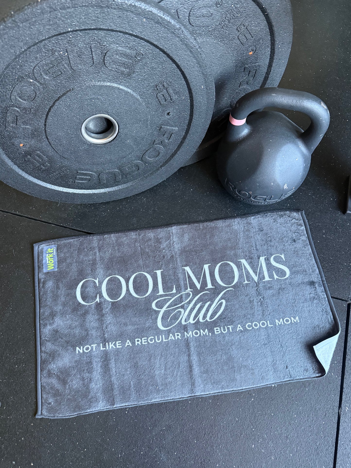 Kettlebell and weight plates on a surface with a 'Cool Moms Club' towel.