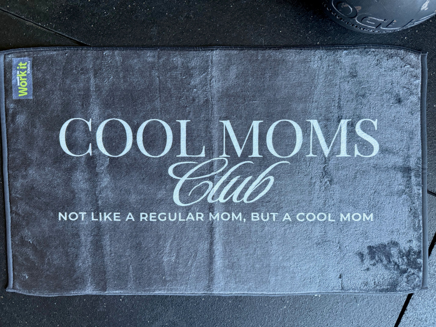 Textile product with 'Cool Moms Club' text on a textured surface