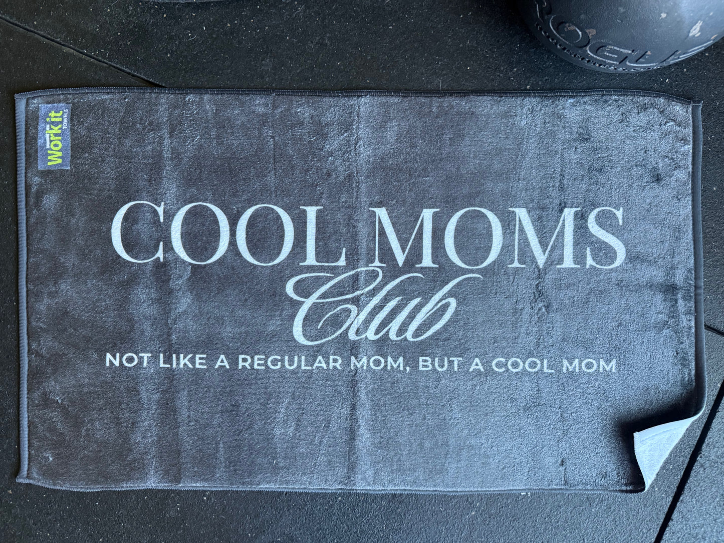 black gym towel with 'Cool Moms Club' text on a black surface