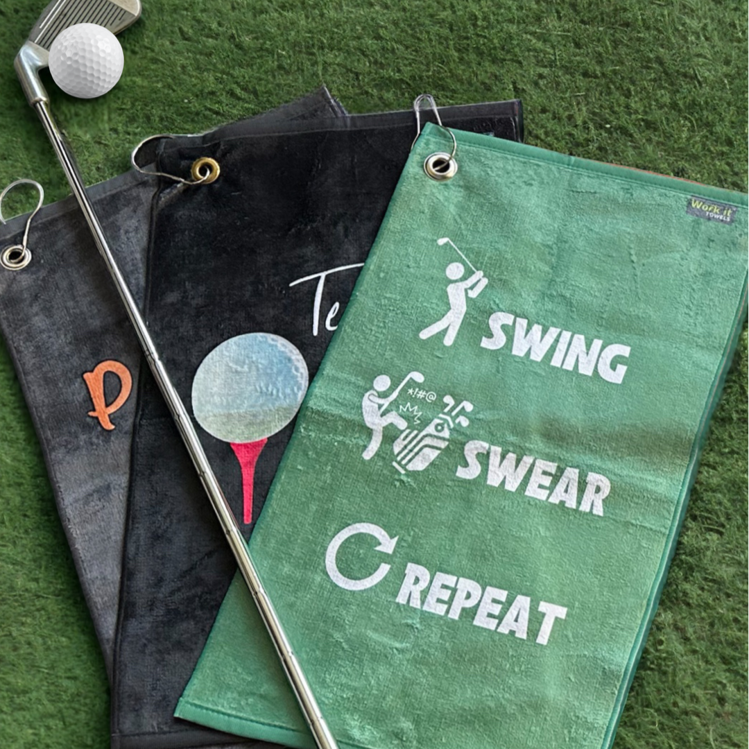 a trio of golf towels with the 'swing swear repeat' design in green atop the other towels. 