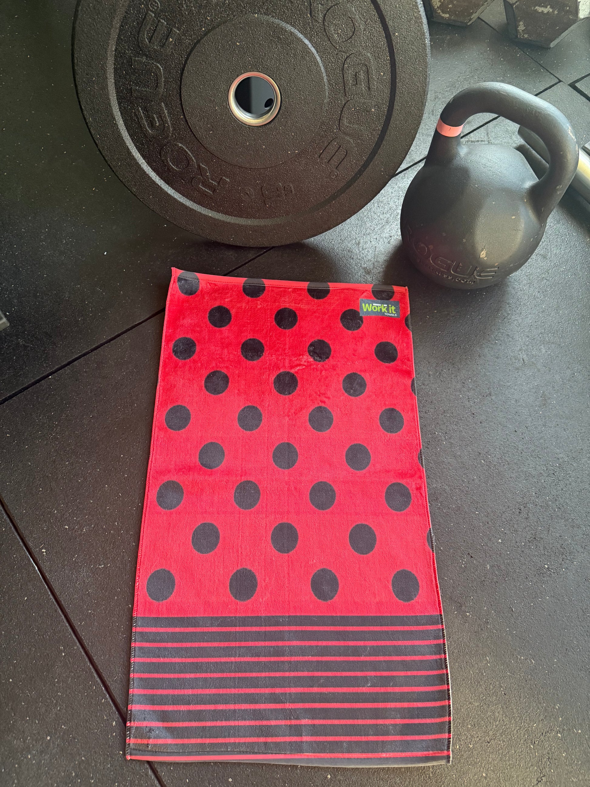 Red towel with black polka dots and stripes on a dark surface with gym equipment.