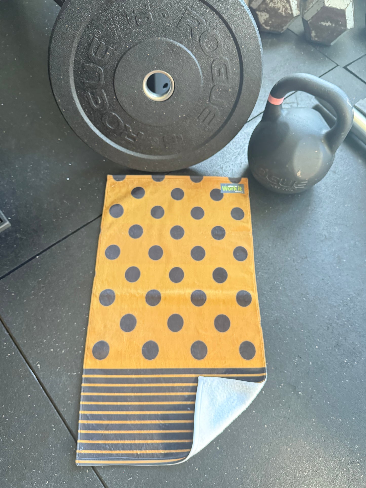 gold owel with black polka dots on a black surface with gym equipment.