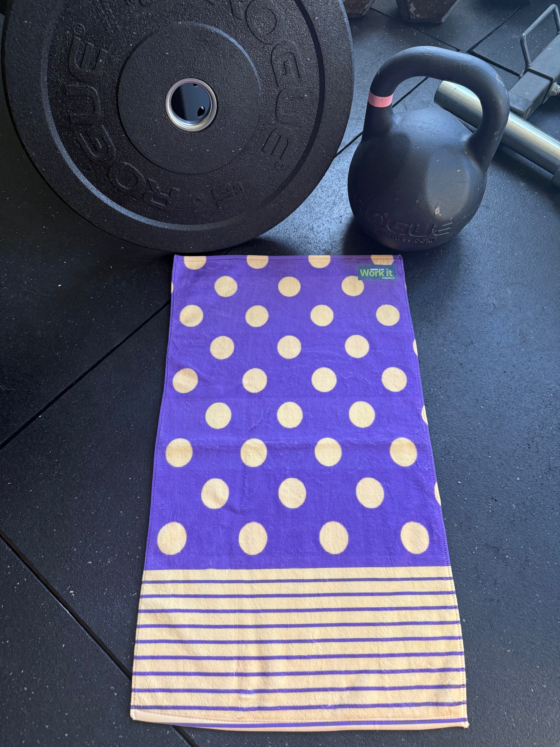 Purple towel with gold polka dots and stripes on a gym floor with weights.