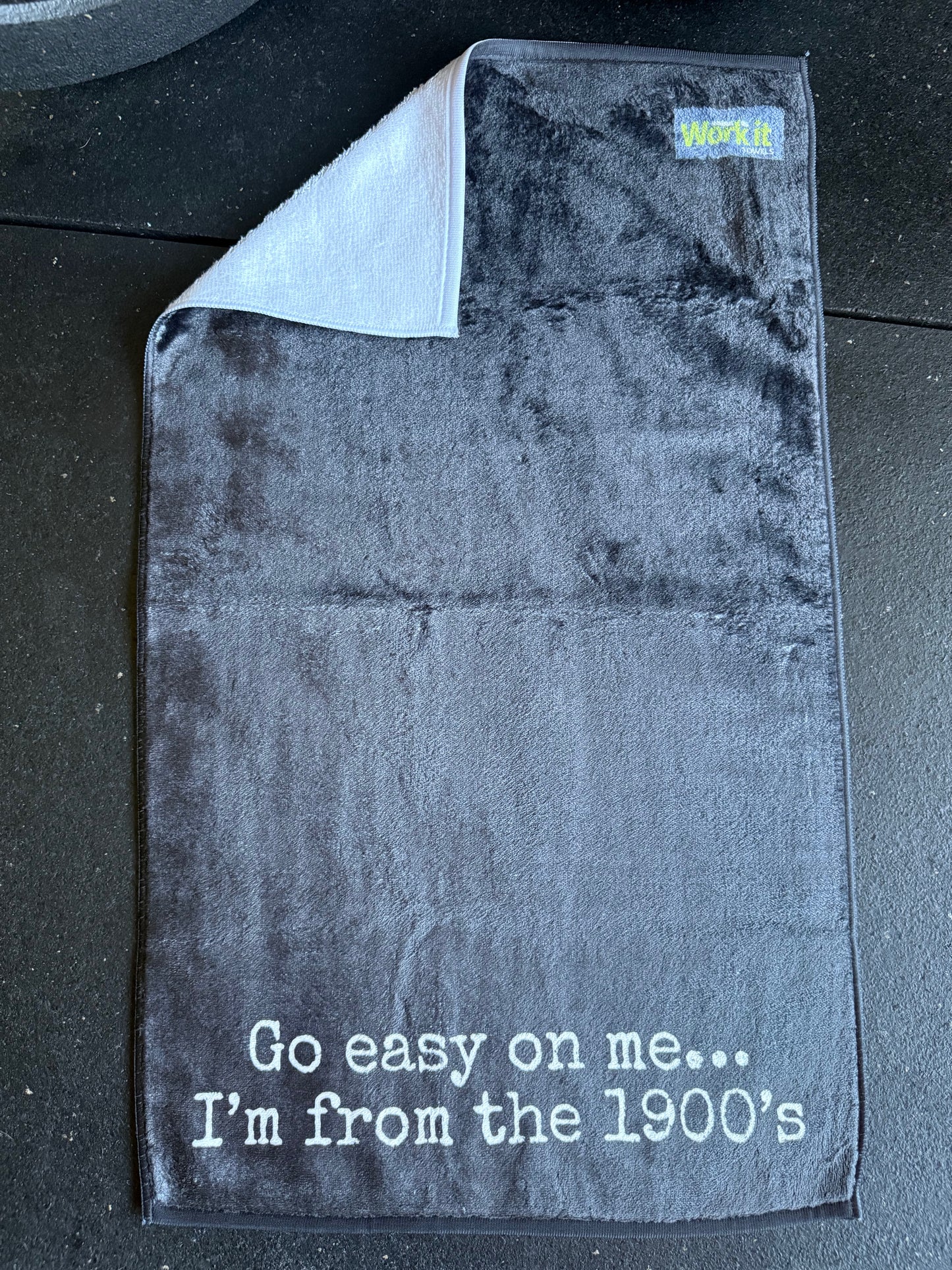 Black gym towel with text, 'go easy on me...I'm from the 1900's' on a black surface
