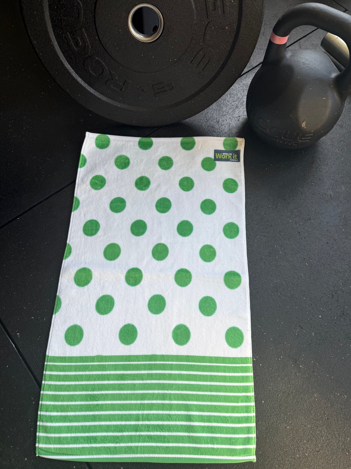 Green and white polka dot towel on a black surface with gym equipment.