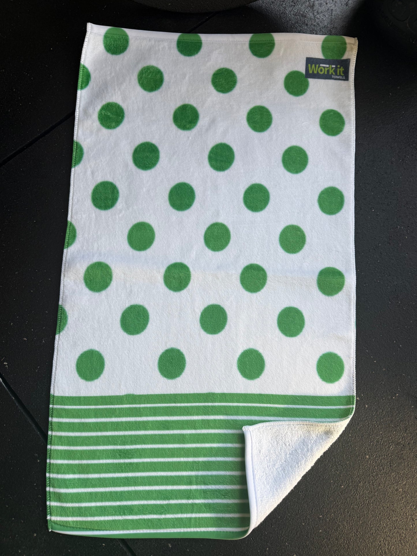 Green and white polka dot towel with a brand label on a dark surface