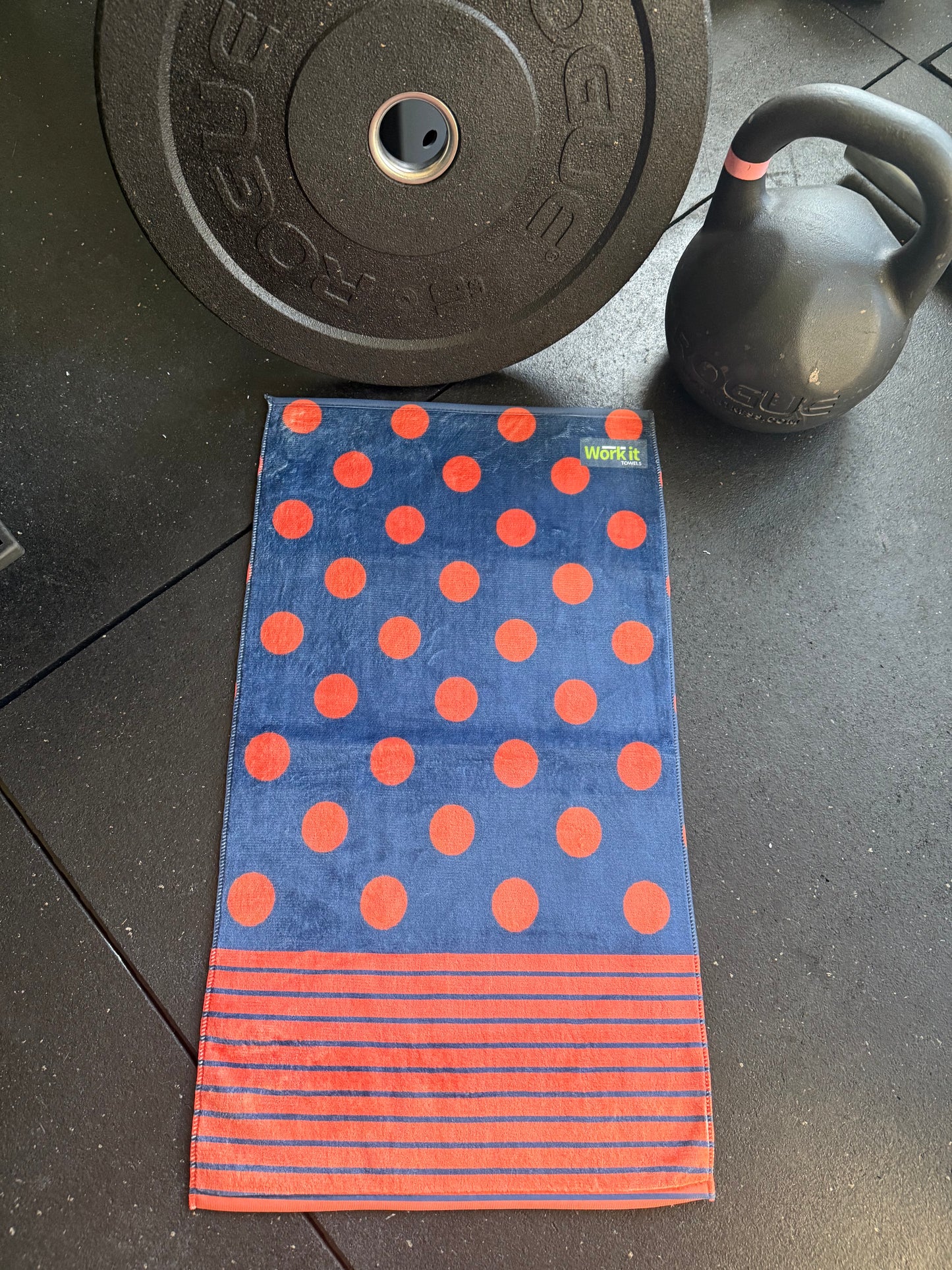 Blue towel with red polka dots and stripes on a black surface with gym equipment.