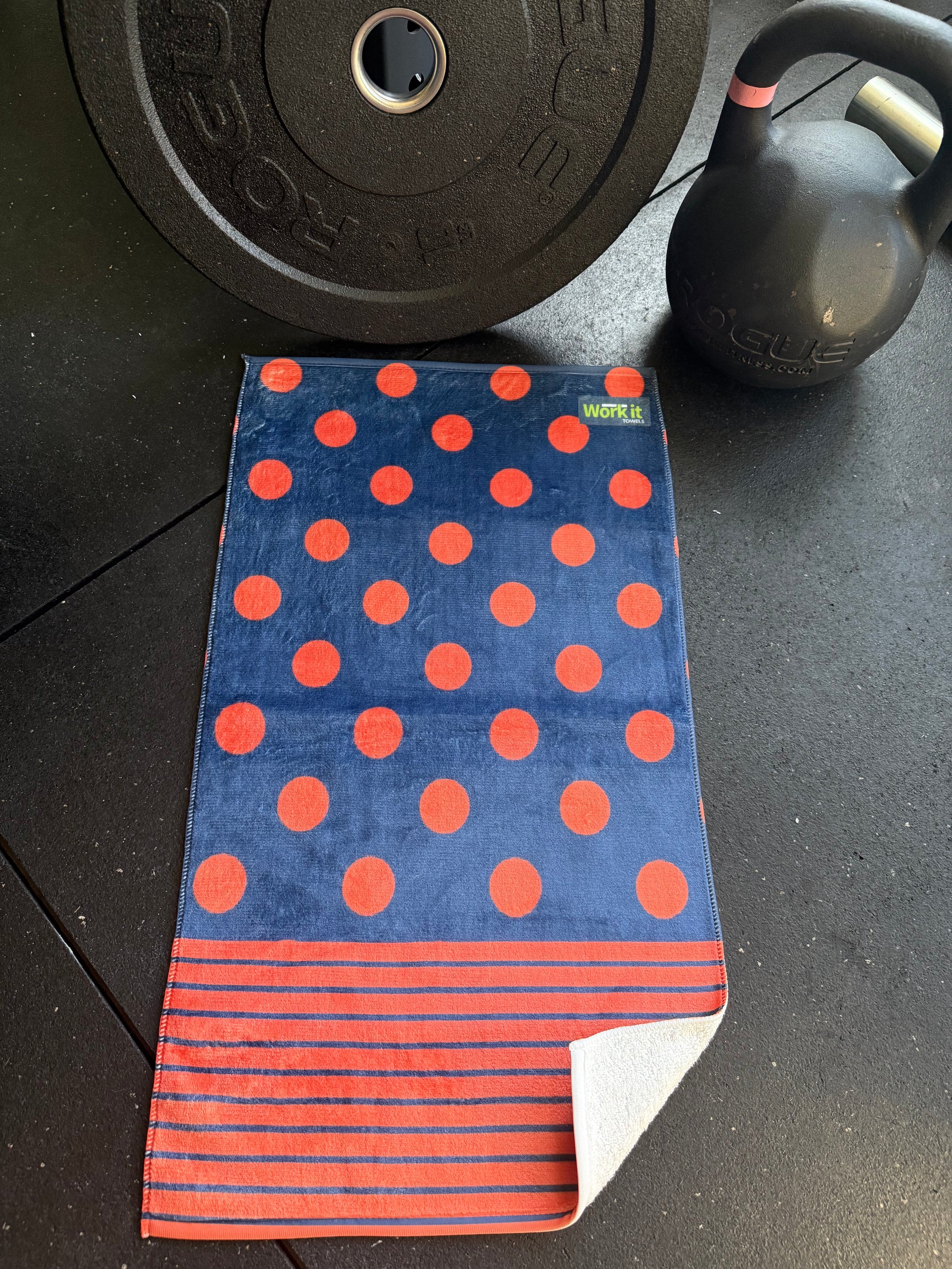 Blue towel with red polka dots and stripes on a black surface with gym equipment.