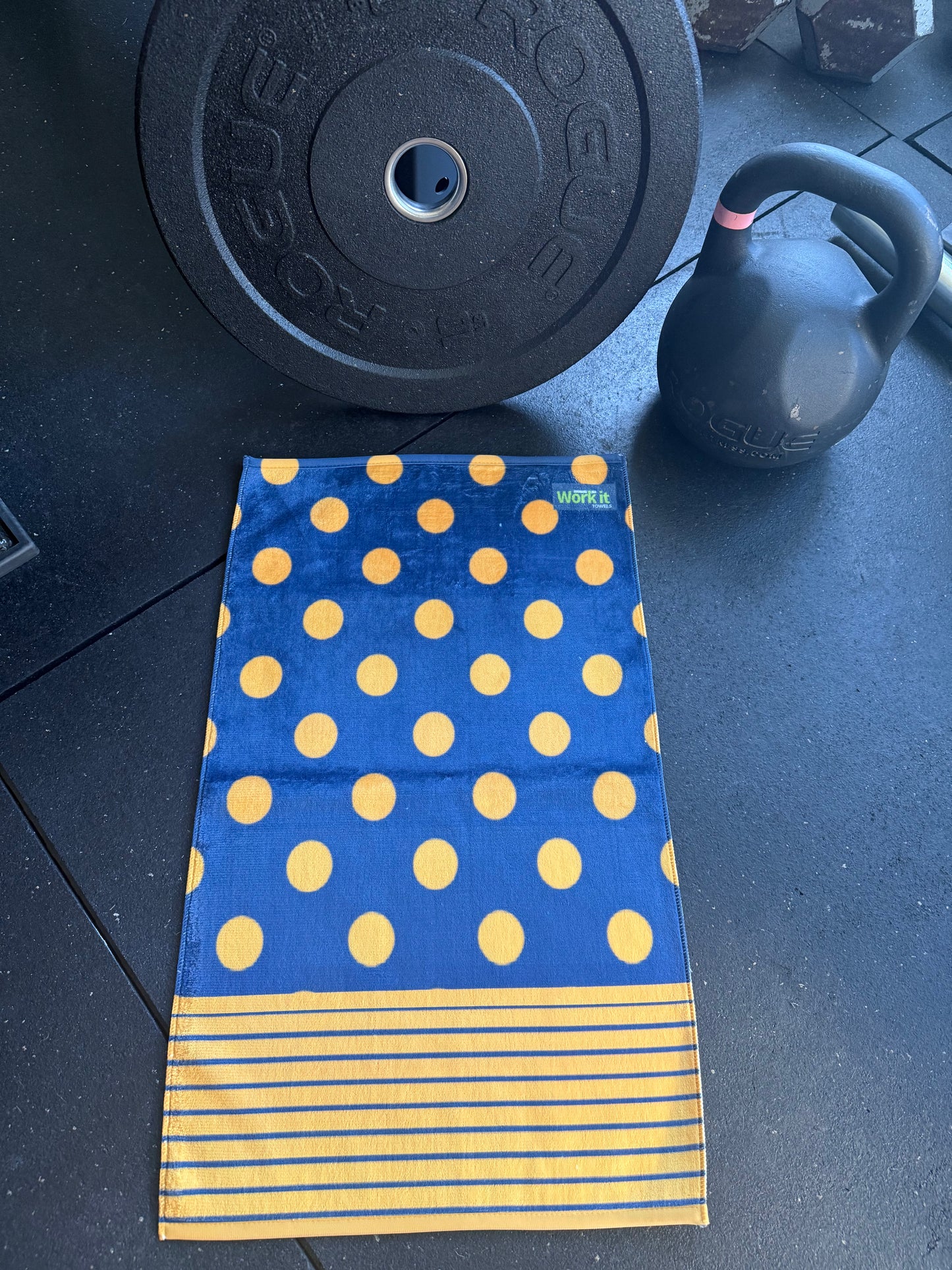 Blue towel with yellow polka dots and stripes on a gym floor with weights and a kettlebell.