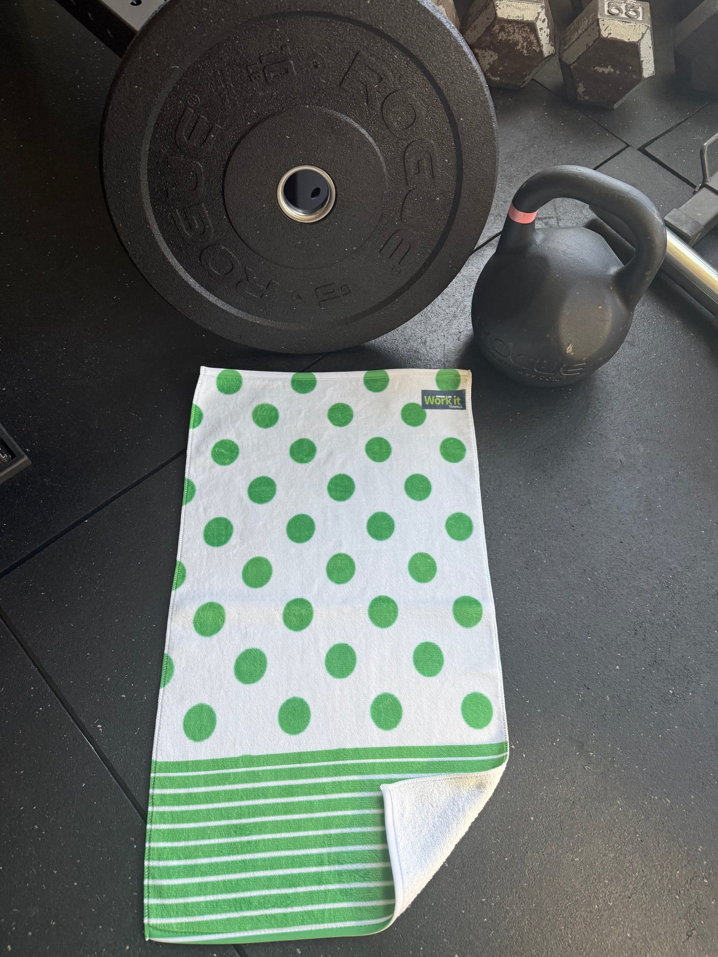 Green and white polka dot towel on a black surface with gym equipment in the background
