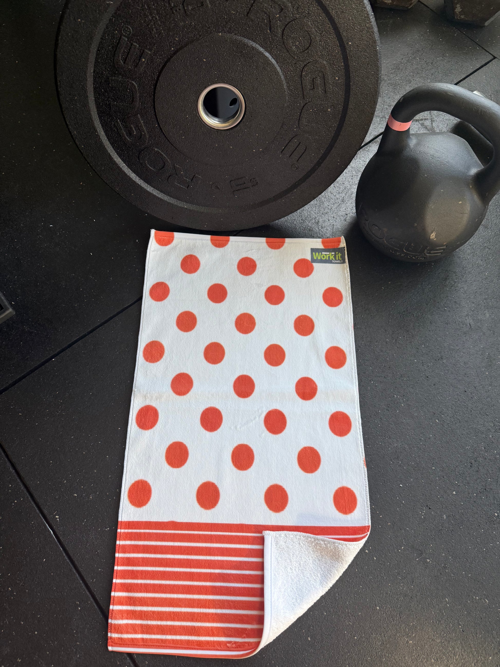Red polka dot towel on a black surface with a barbell and kettlebell in the background