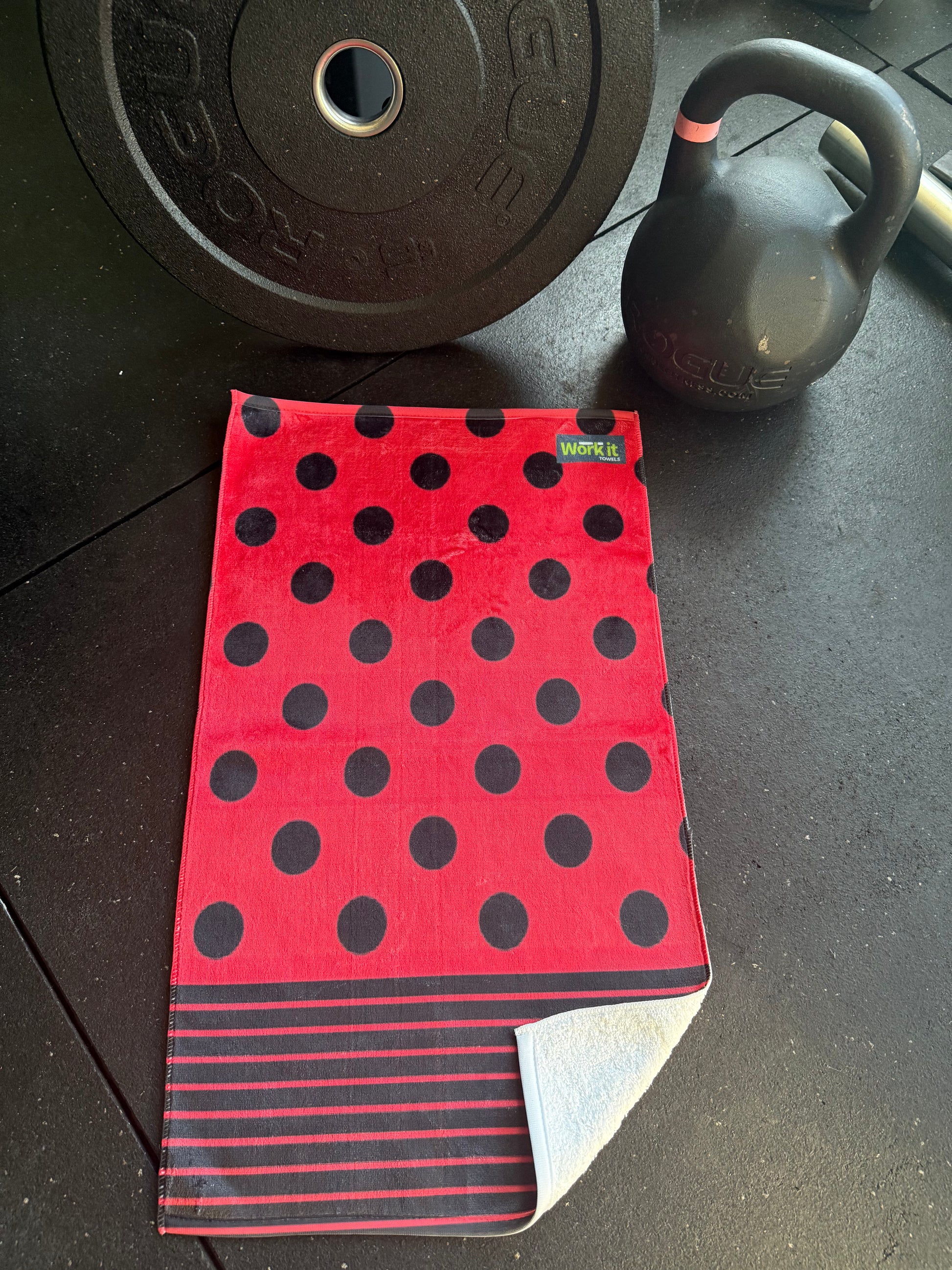 Red towel with black polka dots on a dark surface with weights in the background