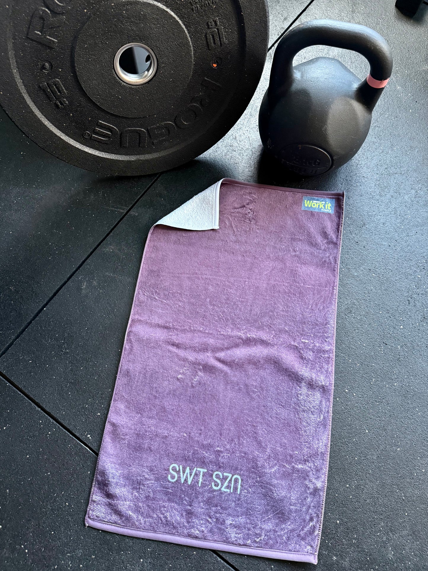 Purple towel with 'SWT SZN' branding on a gym floor with weights in the background