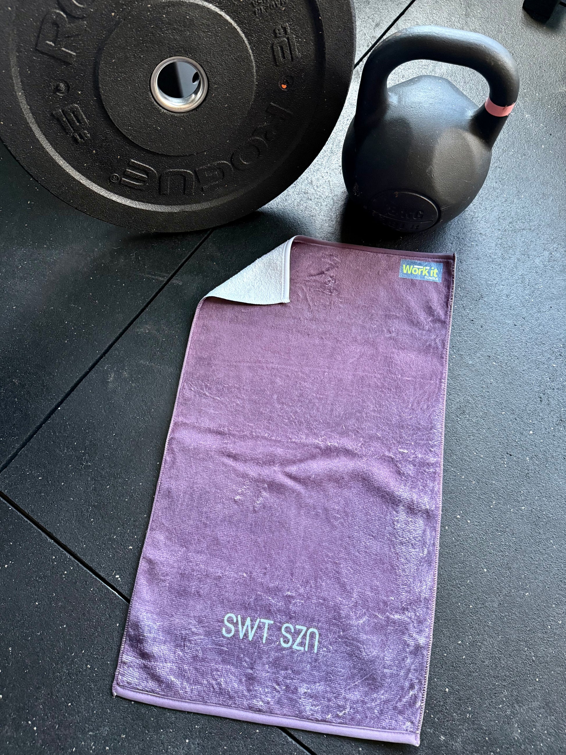 Purple towel with 'SWT SZN' branding on a gym floor with weights in the background