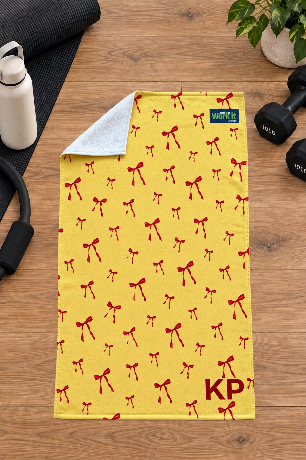 Yellow and red bow personalized gym towel with custom 'KP' initials, one corner folded back to show the soft white terry reverse side.