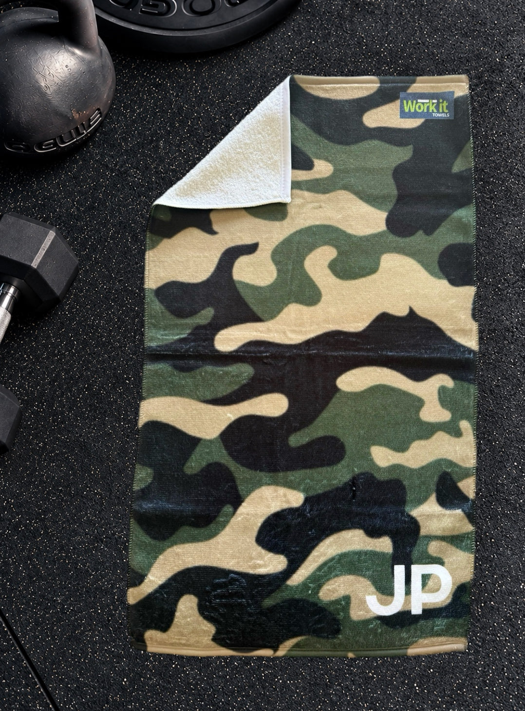 Green camouflage personalized gym towel with custom 'JP' initials, one corner folded back to show the soft white terry reverse side.