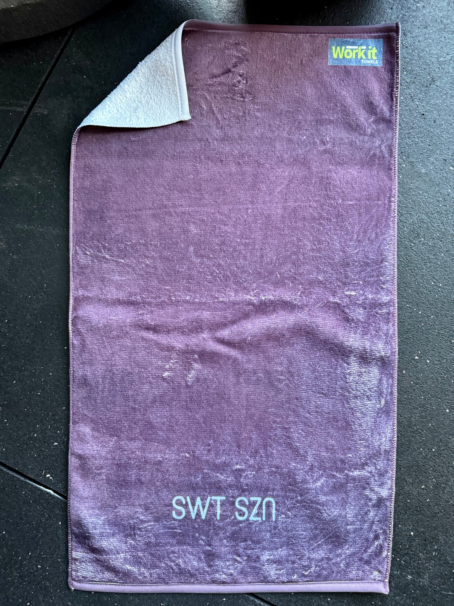 Purple towel with 'SWT SZN' text on a dark surface