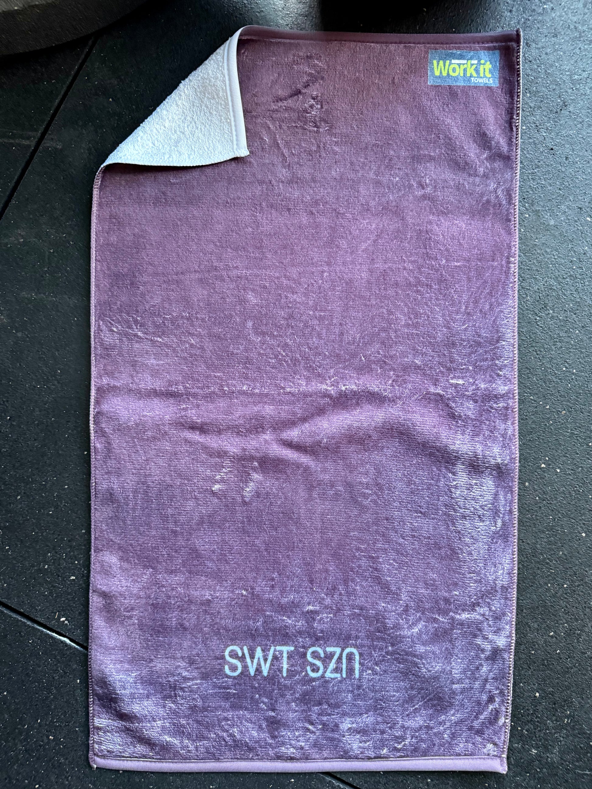 Purple towel with 'SWT SZN' text on a dark surface