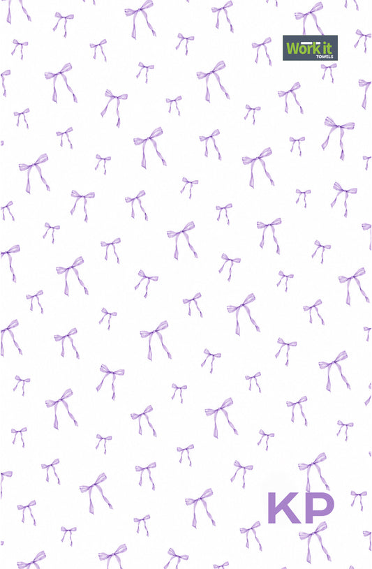 Purple bow personalized gym towel: white with an all-over purple bow print, Work It Towels tag, and custom 'KP' initials in purple at the bottom right.
