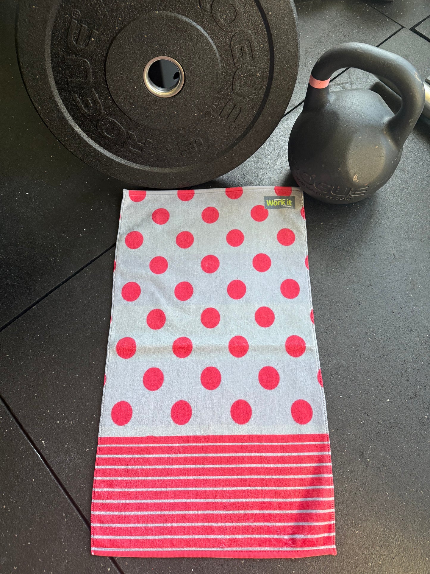 Polka dot towel with red circles and white stripes on a dark floor with gym equipment.