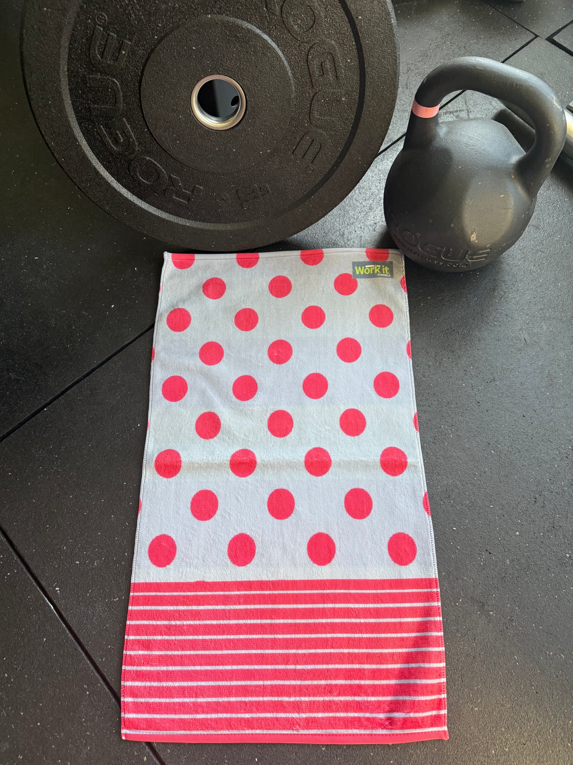Polka dot towel with red circles and white stripes on a dark floor with gym equipment.