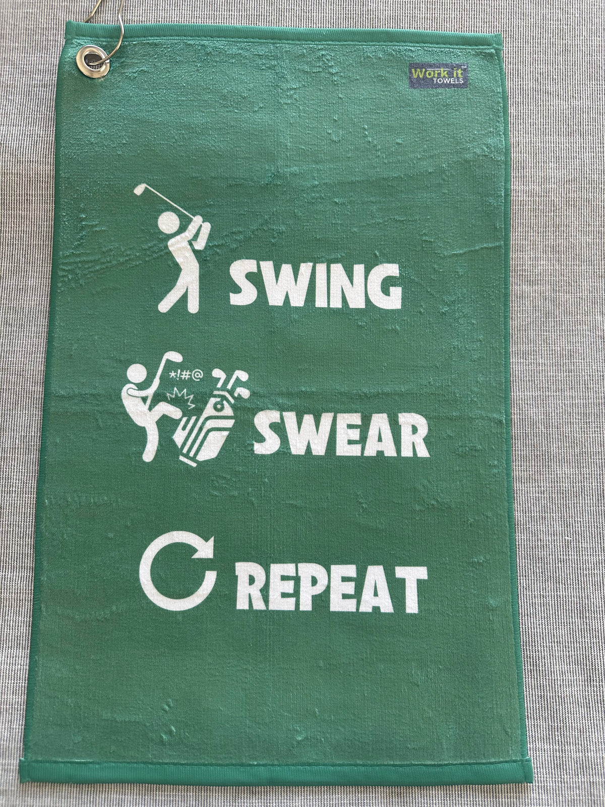 green golf towel with 'swing swear repeat' text and coordinating graphics (golf swinger, kicking clubs, arrow) in white font.  Includes hook and grommet. 