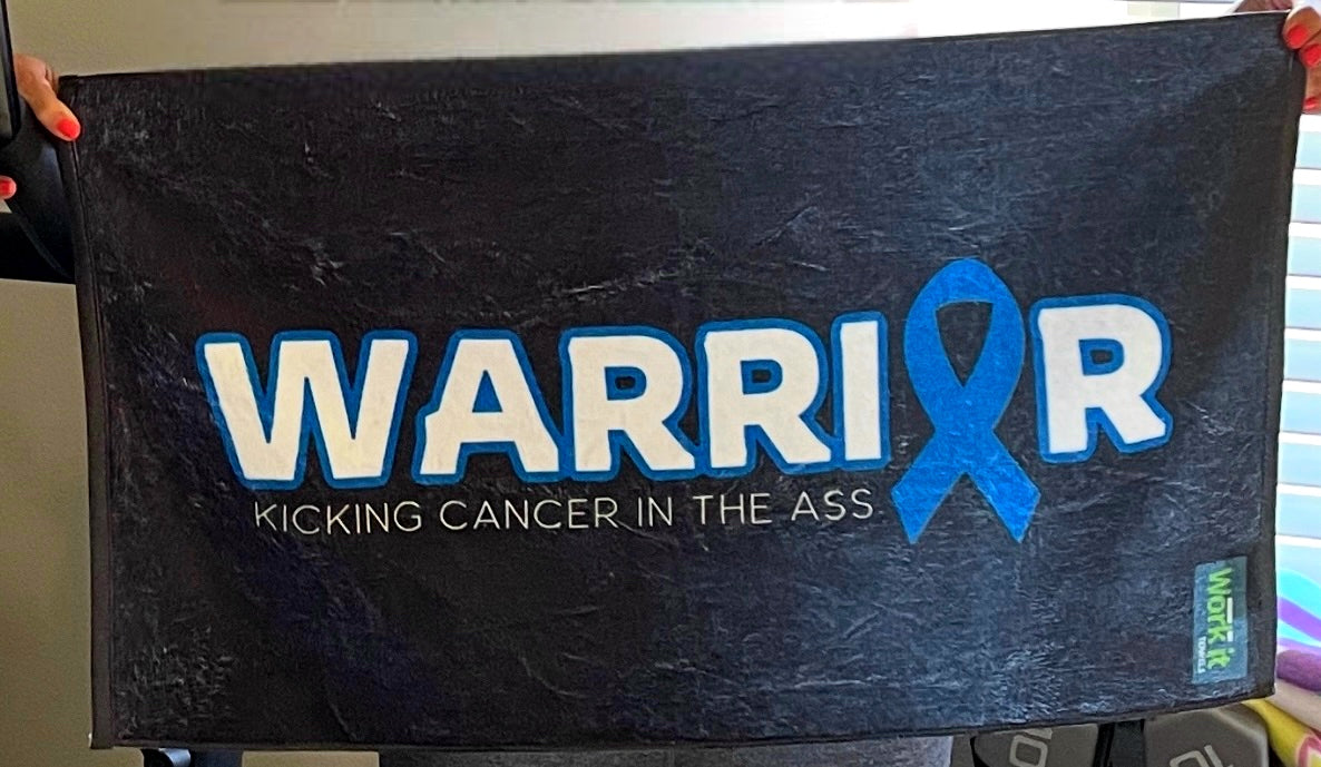 Black towel with 'WARRIOR' and blue ribbon design, held by a person.